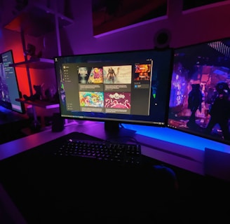 A gaming setup featuring multiple screens with vibrant game-related images illuminated by colorful LED lighting. The environment is dimly lit, highlighting the vivid displays on the monitors. A keyboard is visible on the desk beneath the central monitor.