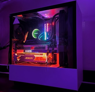 A gaming PC with a transparent side panel reveals internal components illuminated by RGB lighting. Key components visible include a graphics card, cooling system, and motherboard, all surrounded by multicolored LED lights. The case has a minimalistic design, set against a dark background that highlights the vibrant internal lighting.