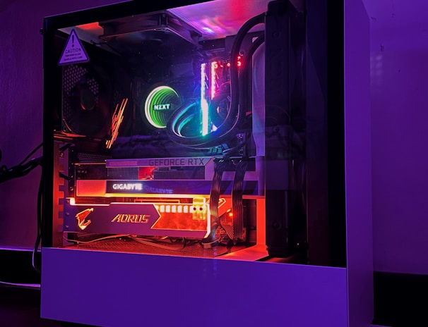 A gaming PC with a transparent side panel reveals internal components illuminated by RGB lighting. Key components visible include a graphics card, cooling system, and motherboard, all surrounded by multicolored LED lights. The case has a minimalistic design, set against a dark background that highlights the vibrant internal lighting.