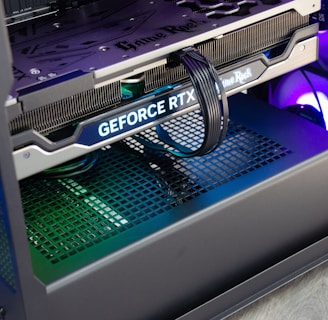 A close-up view of the interior of a computer casing showcasing a high-end graphics card with 'GeForce RTX' branding. The graphics card is secured in its slot, and several power cables are attached. The background reveals cooling fans illuminated with RGB lighting.